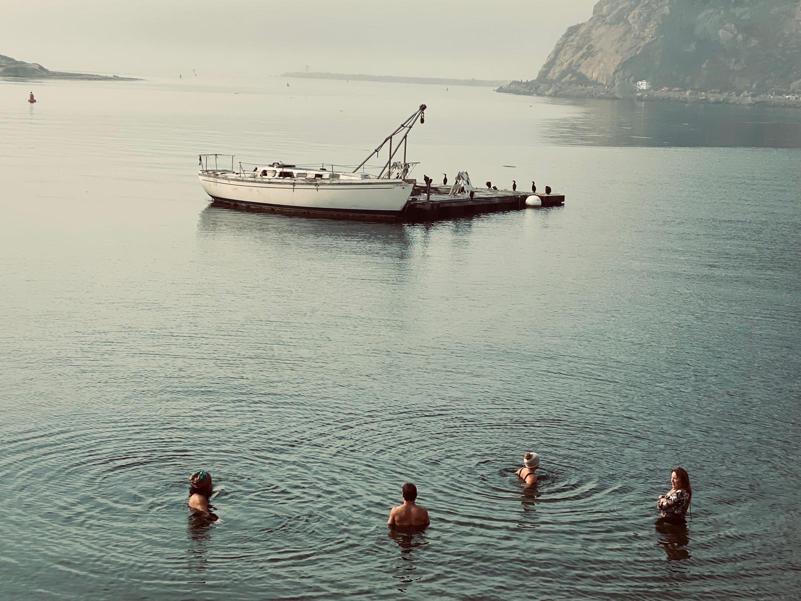 Four bathers in soft grey water beside a moored boat on a misty morning
