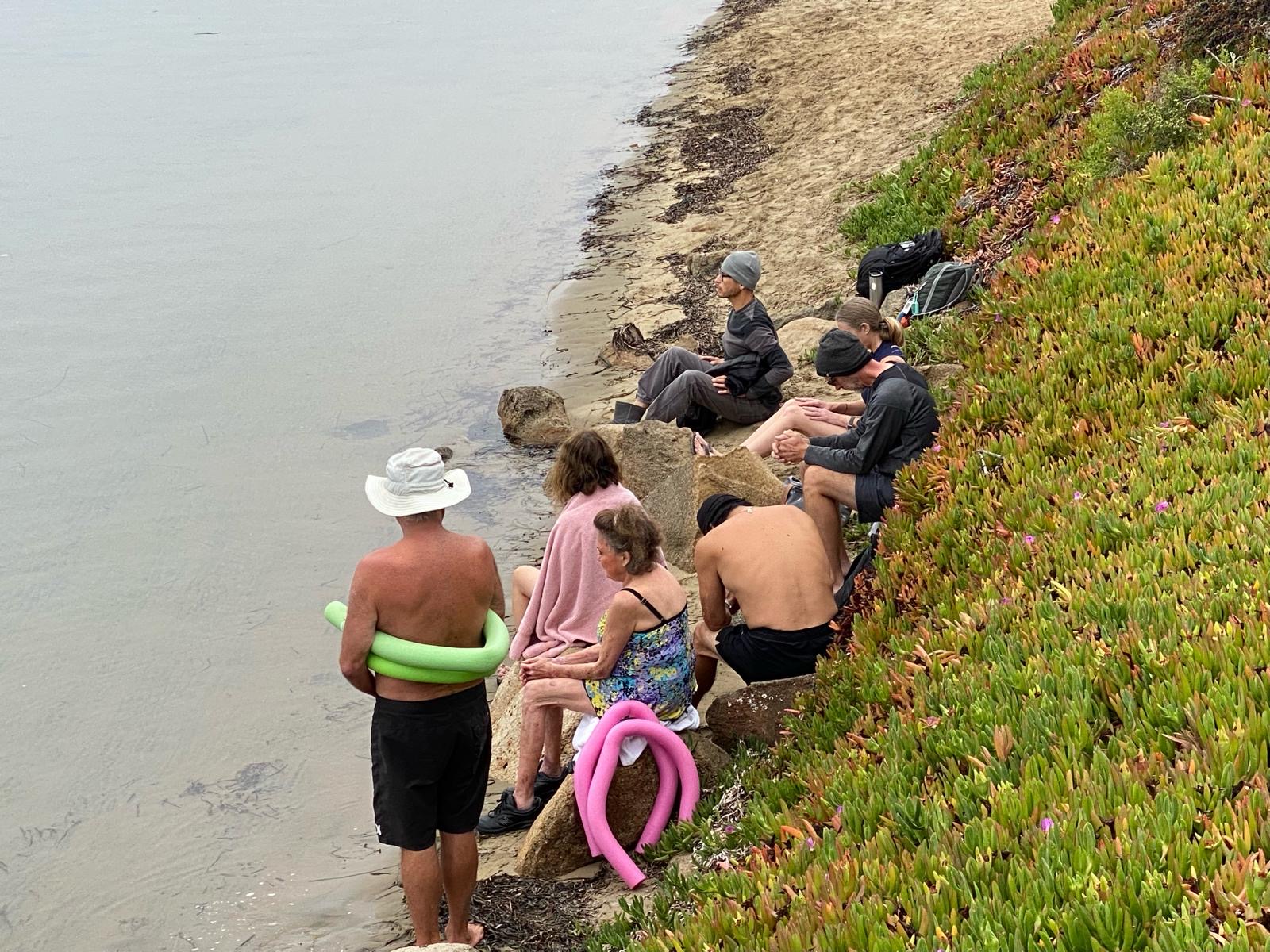 Members sitting on the rocks in towels and blankets, warming up after a dip