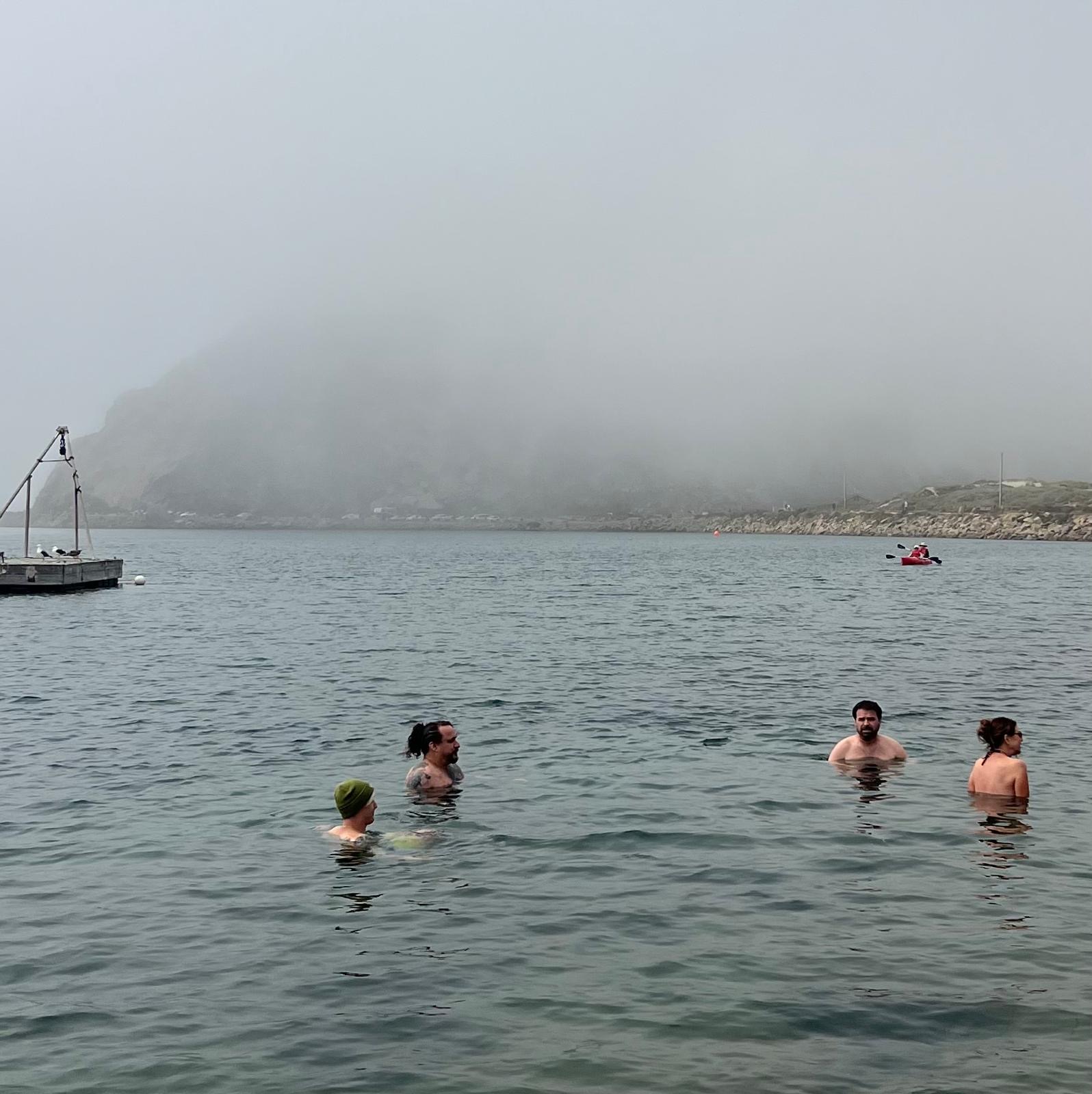 Swimmers in the bay with Morro Rock disappearing into thick fog